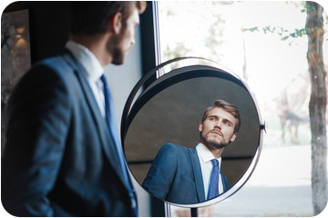 Homme en costard bleu ciel regardant son reflet dans un miroir rond et réfléchi à sa vie